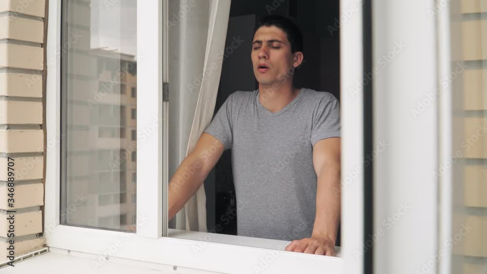 A sad looking guy standing near the open window and tries to calm down. Problems and depression A sad looking guy standing near the open window and tries to calm down. Problems and depression