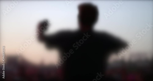 blurred silhouette of young man with cap waving hands at music festival