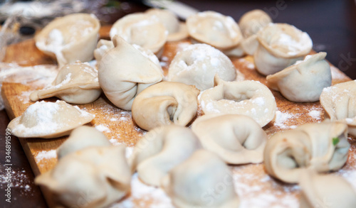 Raw homemade dumplings with minced meat on wooden board on table, sprinkled with flour. Close up view of traditional Russian pelmeni. Selective focus
