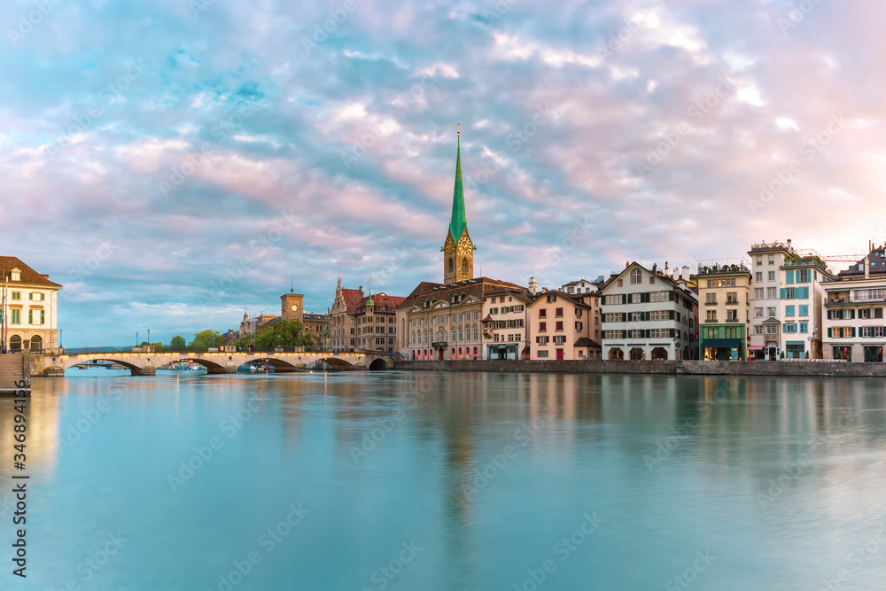 Famous Fraumunster church with its reflection in river Limmat at pink sunrise in Old Town of Zurich, the largest city in Switzerland