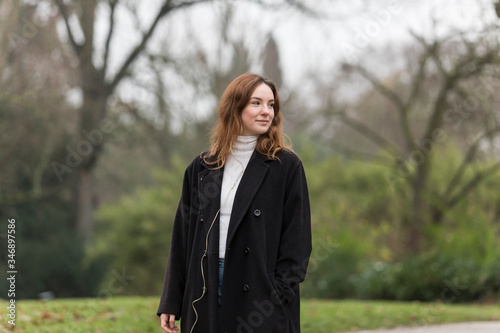 Young Woman in Long Black Wool Coat Looking Away in Public Park