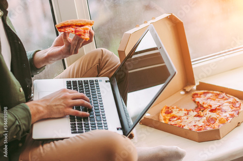 Closeup stylish businessman freelancer eat slice of tasty pizza and using laptop for distance work from home. Hipster man hold takeaway italian fast food snack in hand, type on keyboard. Lunch break