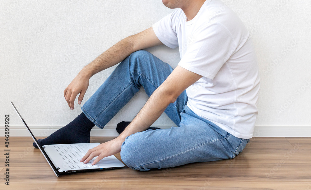 床に座ってノートパソコンを使う男性