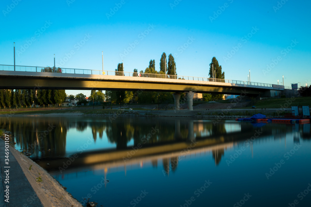 In the light of the setting sun, the bridge is reflected from the water of the river