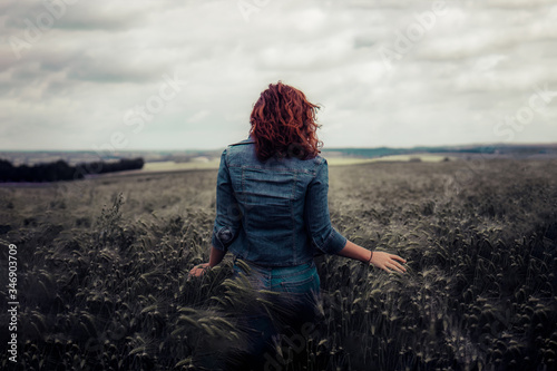 young red haired woman walking away in a wheat field