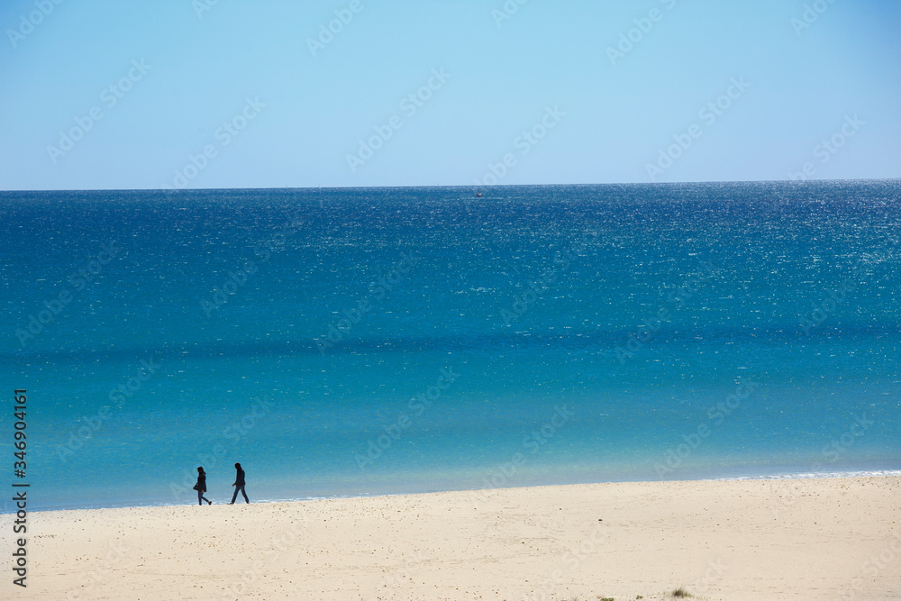 spiaggia della Sardegna con sfondo mare e cielo e due persone in lontananza che passeggiano