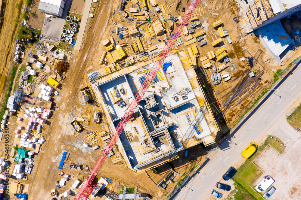 Aerial view of tower lifting crane and concrete frame of tall apartment residential building under construction in a city. Urban development and real estate growth concept. Aerial view of tower lifting crane and concrete frame of tall apartment residential building under construction in a city. Urban development and real estate growth concept.