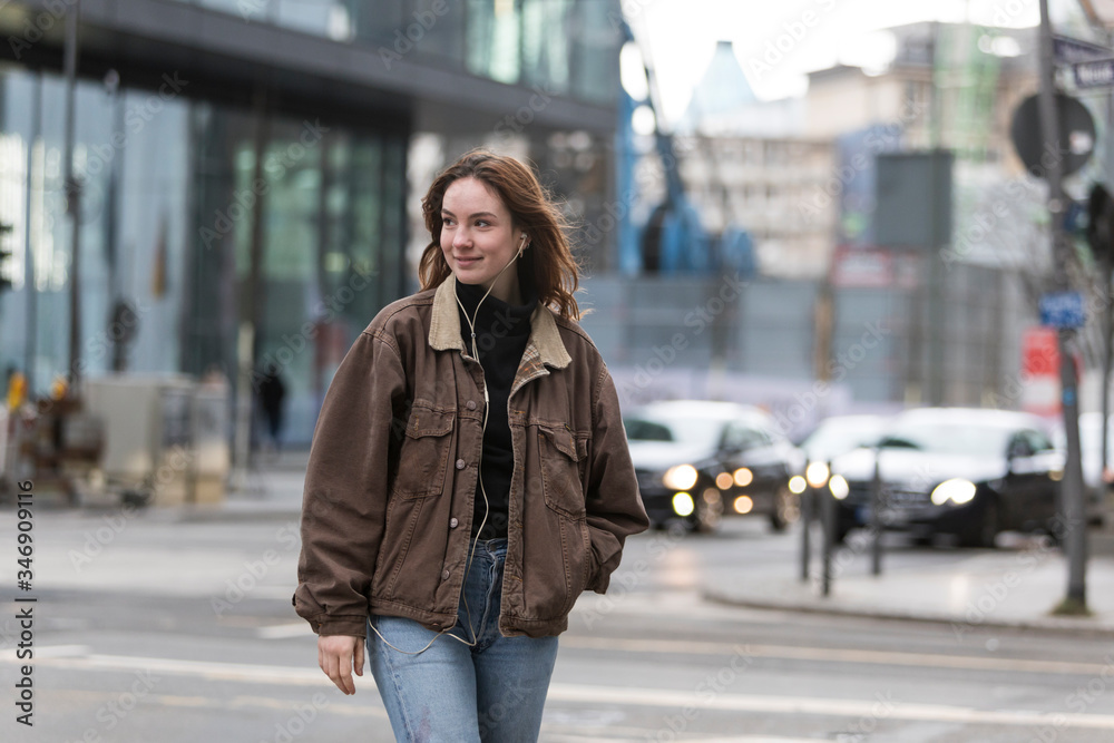 Fototapeta premium Young Woman Listening to Earphones Smiling with Head Turned on Street
