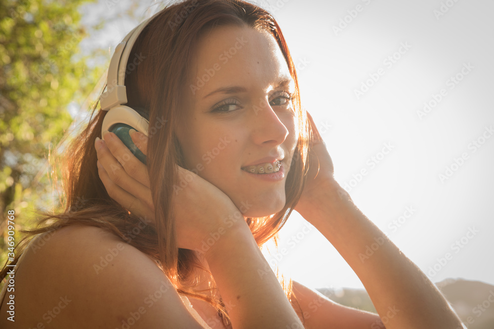 Millennial joven de pelo rojo disfrutando de videochat al aire libre en tiempos de crisis y encierro, usando auriculares y movil o tablet para conectarse con el mundo.