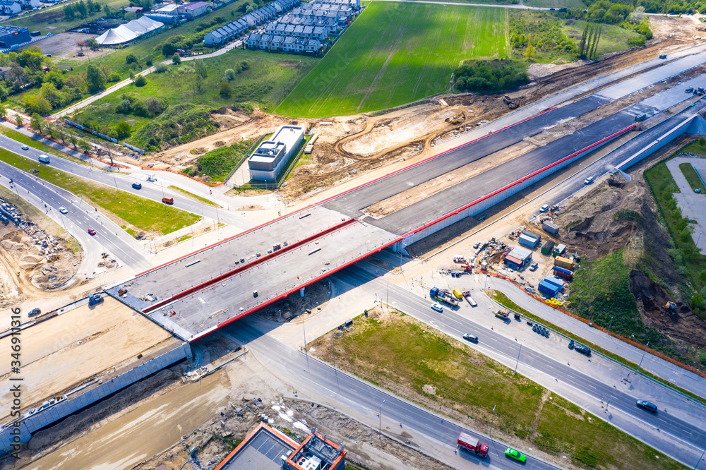Fototapeta premium Aerial panorama top down view of an unfinished asphalt covered road with dirt, tracks of heavy machinery at construction site. The road to nowhere.