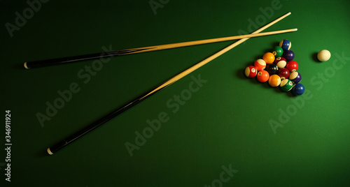 billiard cues and pyramid of multicolored pool balls on green billiard table