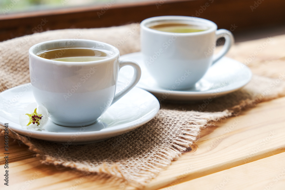 two white cups on a saucer on a linen napkin on a light wooden table.