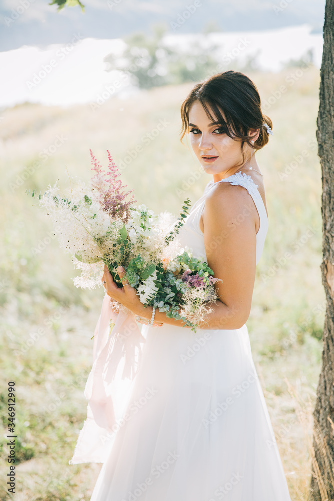 Bride in a luxurious white wedding dress in nature at sunset Bride in a luxurious white wedding dress in nature at sunset