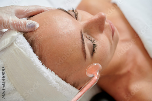 Young female receiving galvanic facial treatment in spa cosmetologist wearing gloves professional services.