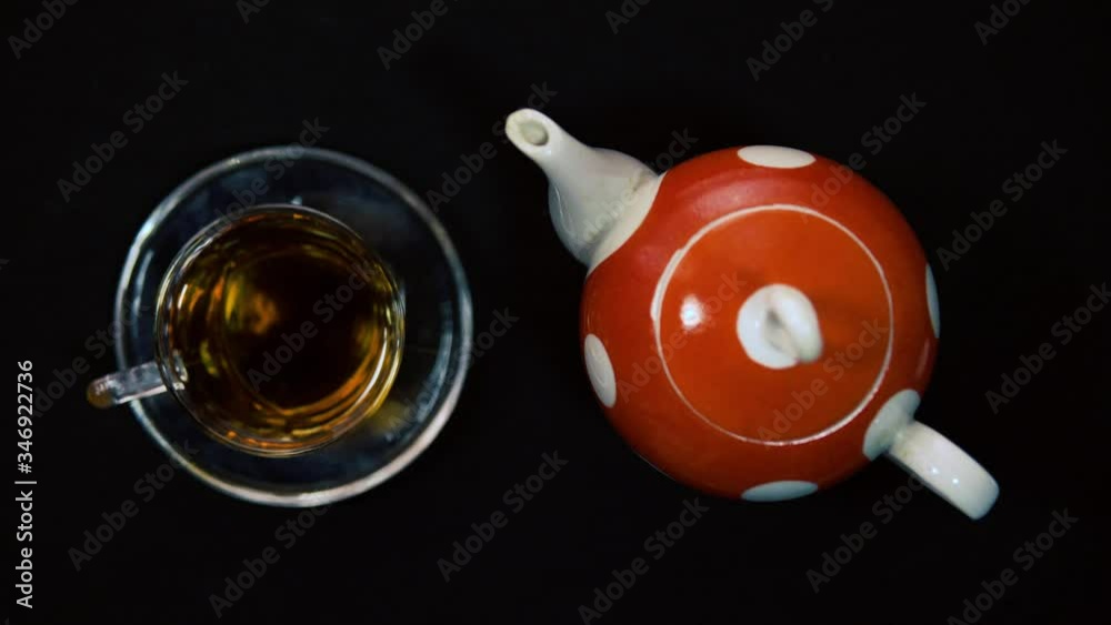 Tea ceremony. A male hand closes the ceramic lid of a hot red polished white ceramic teapot next to a glass bowl for a bowl. Black background, oncoming light 4k Tea ceremony. A male hand closes the ceramic lid of a hot red polished white ceramic teapot next to a glass bowl for a bowl. Black background, oncoming light 4k
