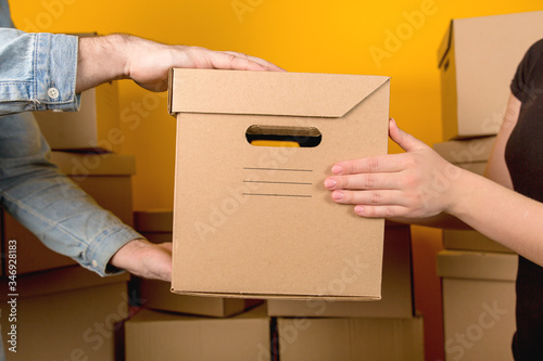 Delivery man handing the customer a cardboard box with a parcel close up on a yellow background