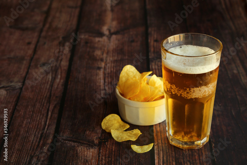 Light foamy beer with potato chips on a wooden table and have copy space.