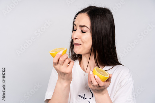 Beautiful girl with dark hair in white t-shirt eating fresh sour lemon