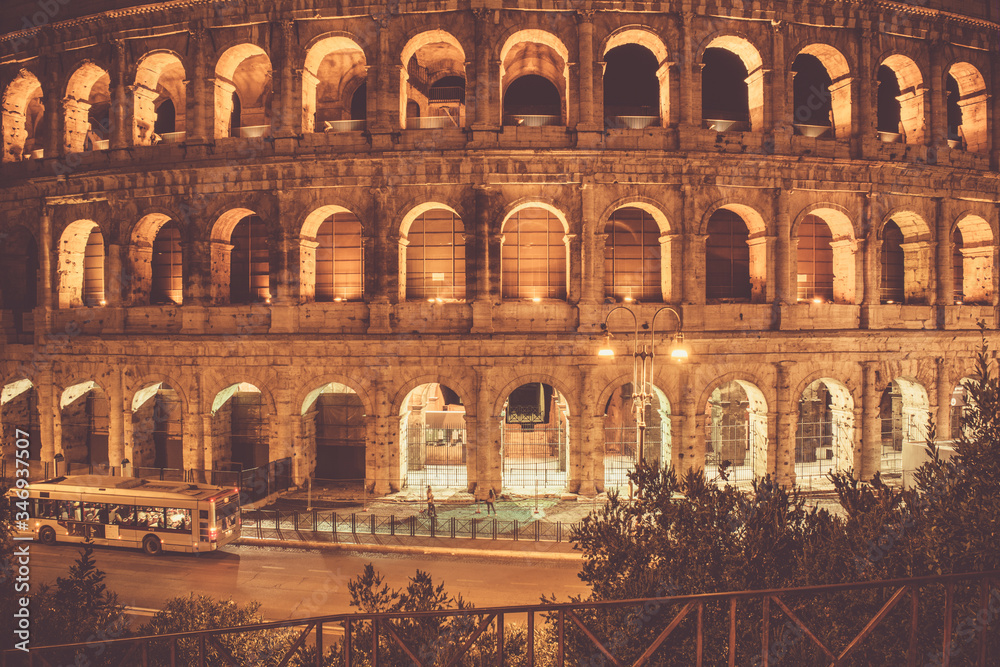 Fototapeta premium night Coliseum with windows lit from the inside and a passing bus
