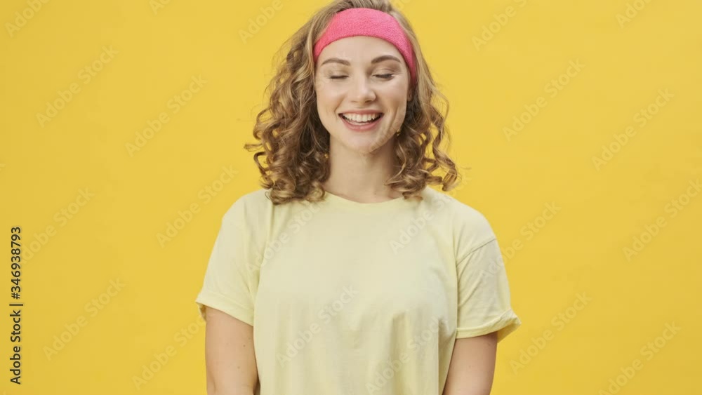 A beautiful young athletic woman in sportswear is smiling isolated over a yellow background in studio A beautiful young athletic woman in sportswear is smiling isolated over a yellow background in studio