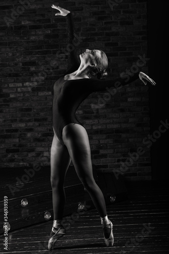 Fototapeta Naklejka Na Ścianę i Meble -  Beautiful young female classical ballet dancer on pointe shoes wearing a black leotard and skirt on a brick background