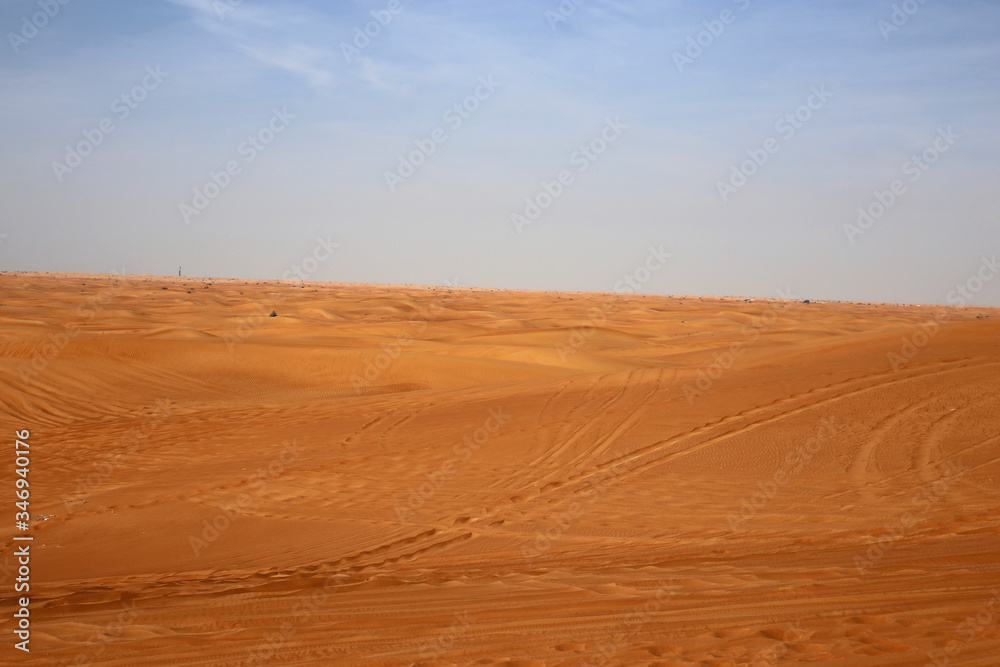 Red sand dunes in Sharjah, UEA during a sunny day. A lot of sand and plenty of tire marks and some footprints since there has been tourists doing dune bashing, walking and enjoying the Middle East.