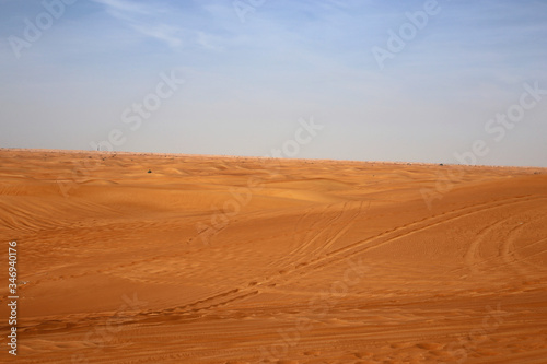 Red sand dunes in Sharjah, UEA during a sunny day. A lot of sand and plenty of tire marks and some footprints since there has been tourists doing dune bashing, walking and enjoying the Middle East.