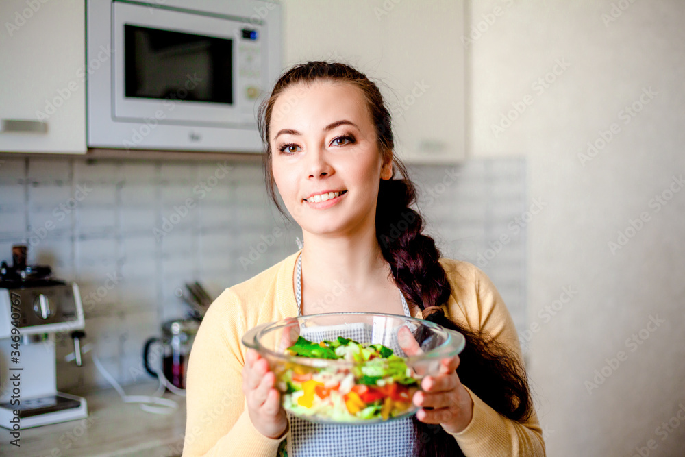 Young brunette woman making healthy food on the dinner table in the kitchen. Female cooking fresh vegan salad with green vegatable