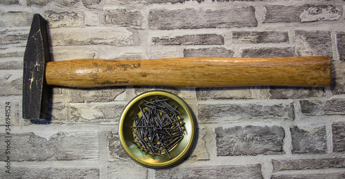 Black nails on a metal stand with a hammer on a brick wall background.
