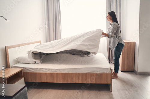 Charming young female person making her bed photo