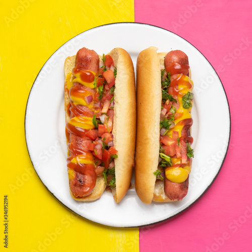 Hot dog with pico de gallo salad on pink and yellow background