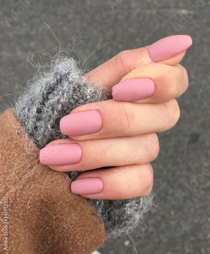 Woman's hand with freshly made pink manicure. Powder light pink nails, mohair wool sweater, grey background.