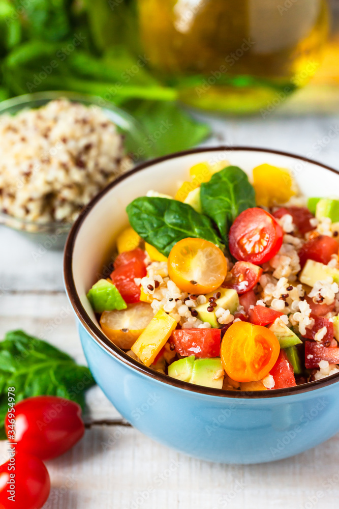 Concept of healthy food, clean eating, low calories delicious meal. Salad with quinoa and fresh vegetables with olive oil in blue bowl. Tomato, avocado, spinach. Close up wooden background