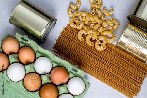 eggs in a box, canned food, macaroni, spaghetti on a gray background form a grocery basket, essential food,