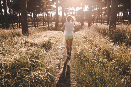 Giovane ragazza si allena e corre in solitudine nel parco in mezzo alla natura illuminata dalla luce del sole al tramonto photo