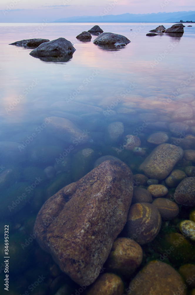 Fototapeta premium Lake Baikal in the summer at sunset. In the foreground is clear water and stones under water.