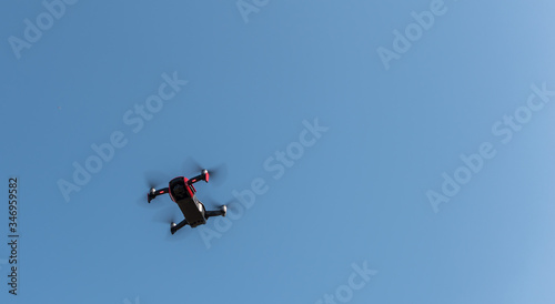 Small sized red drone with high resolution camera hovering in air for aerial photography.