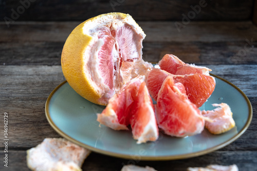 Peeled grapefruit, grapefruit slices lie in a plate on a wooden table.