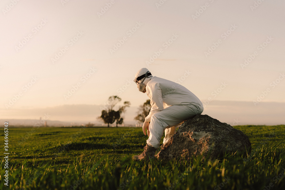 Man wearing protective suit and mask sitting on a rock in the countryside Man wearing protective suit and mask sitting on a rock in the countryside
