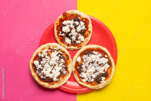 Mexican red sopes with cheese and beans on yellow and pink background