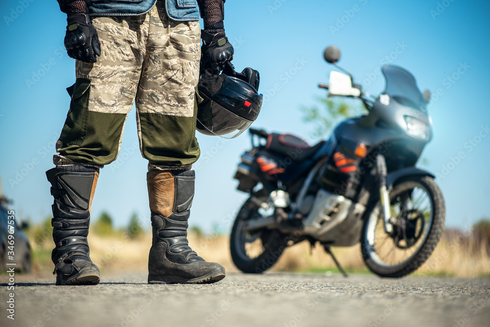 Fototapeta premium Biker with a helmet in hands is standing on the road close up.