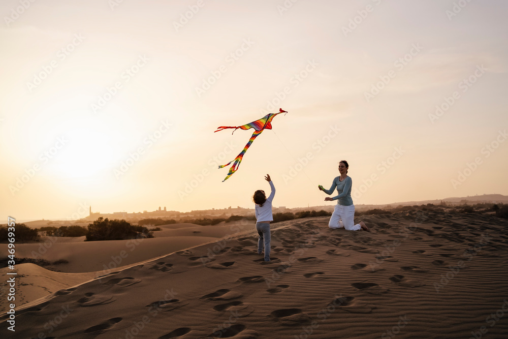 Mother and daughter flying kite in sand dunes at sunset, Gran Canaria, Spain