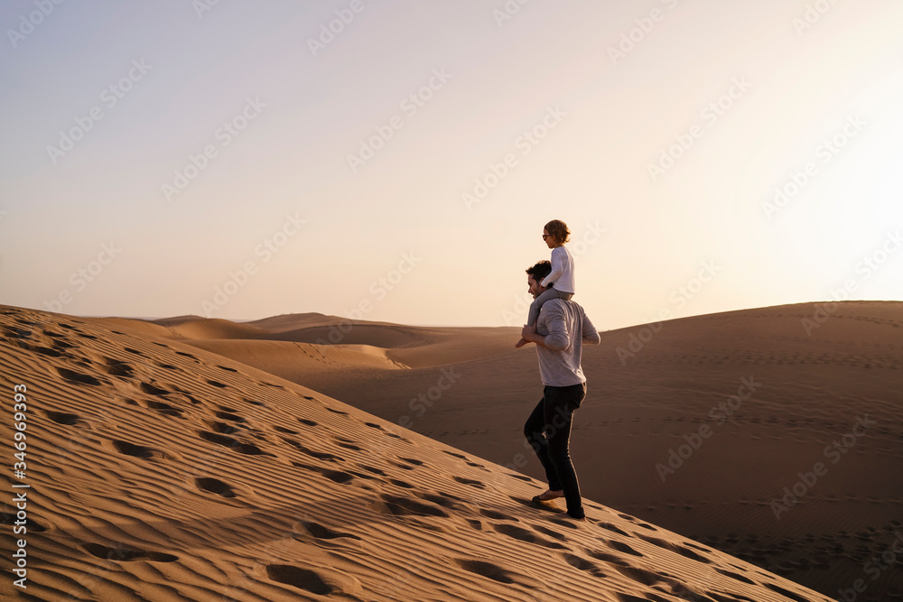Father carrying daughter on shoulders in sand dunes, Gran Canaria, Spain
