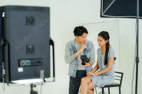 Backstage behind the scene of the photo session: the photographer using digital camera taking picture of the female model in the creative home studio work from home during virus pandemic