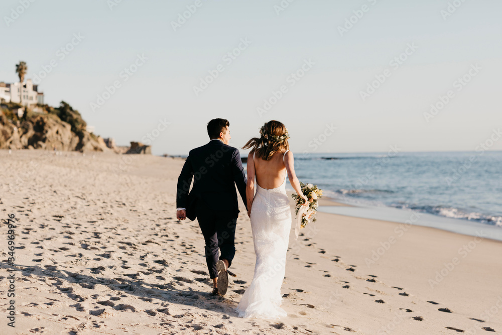 Rear view of happy bridal couple running at the beach Rear view of happy bridal couple running at the beach