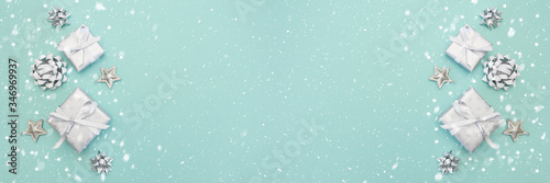 Banner of gifts or present boxes in silver with silver bows and tree ball ornaments and little silver stars, table top view, snowflakes. Composition for Christmas. Turquoise pastel background.