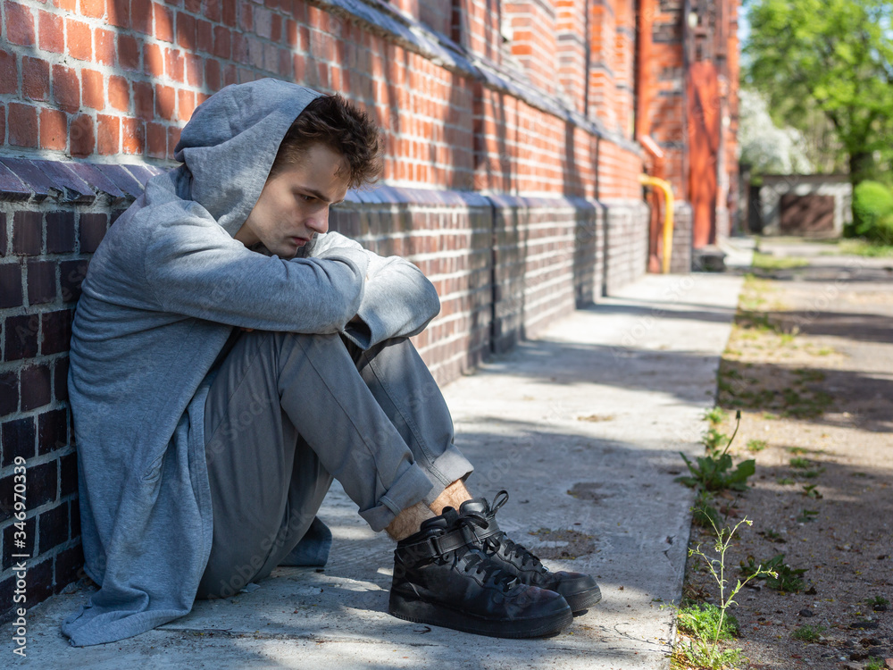 portrait of a lonely sad teenager in a sweatshirt with a hood on the street, problems and psychology of adolescents, concept