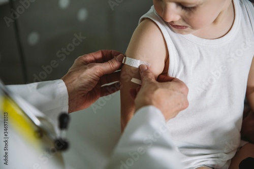 Pediatrist putting band-aid onto arm of toddler after vaccination