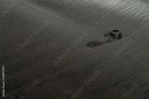 Footprint on a black sand beach macro photography. Human trace on a silky black beach texture with shallow depth of field. Minimalistic black background. Tenerife voulcanic sandy shore.