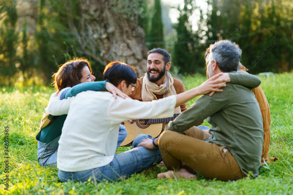 Group of friends playing music and hugging on the grass in the field Group of friends playing music and hugging on the grass in the field